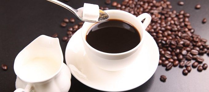 cup of coffee with sugar cube, cream and coffee beans