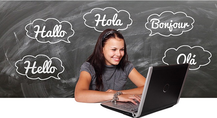 Young student on her laptop with a cloud of  words in different languages written on a chalkboard as an example of a linguistics major