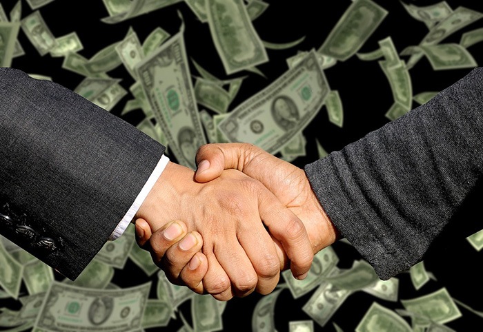 Photo of two men shaking hands with dollars bills in the background as an example of ways to make money writing online