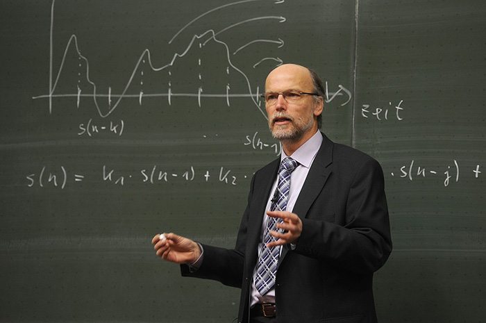 Teacher standing in front of a chalkboard lecturing a class as an example of a retired teacher returning to the workforce