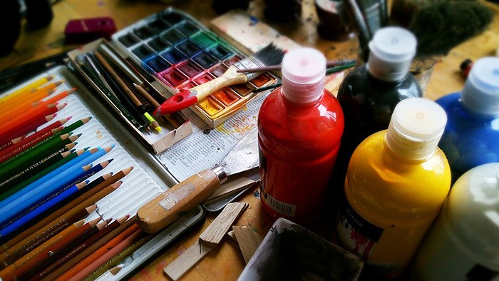 Photo of a cluttered table of art supplies as an example of getting paid to write about art