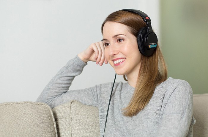 Young woman listening to a pair of headphones as an example of getting paid to write about music