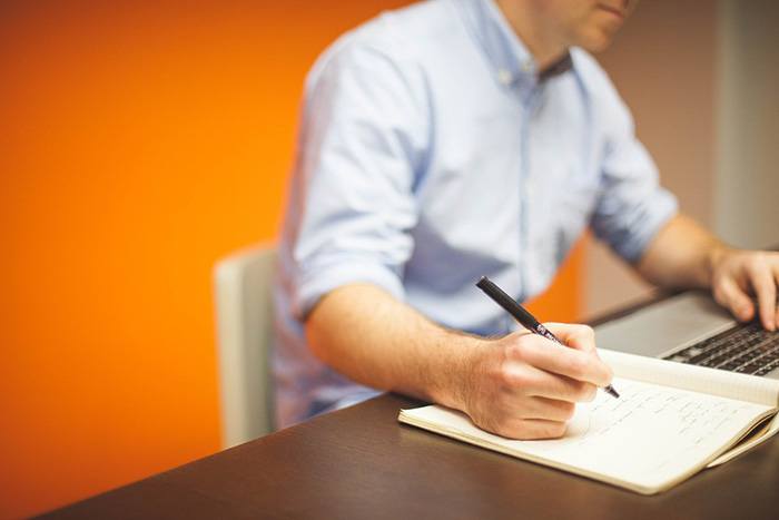 Photo of a man at his computer scribbling on a piece of paper as an example of business articles