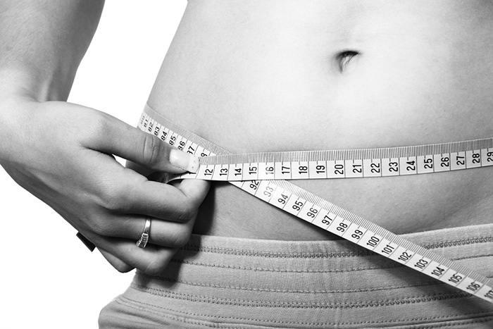 Photo of a woman measuring her waistline as an example of health articles