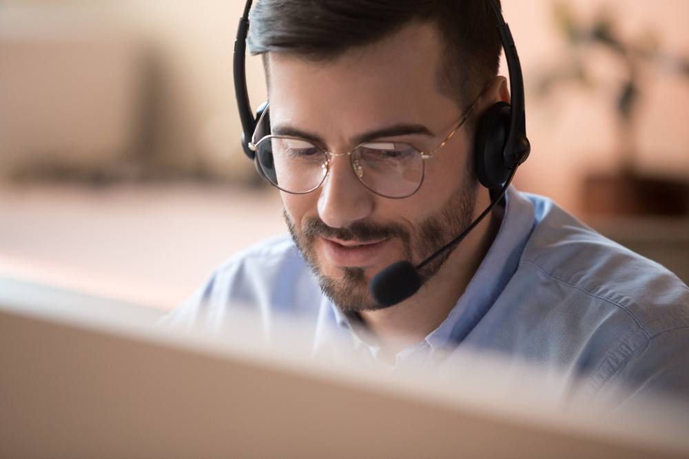 A man sitting on his computer wearing a headset being a telemarketer