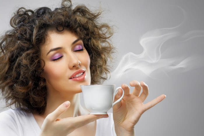 Young woman holding a cup of coffee with her eyes closed.