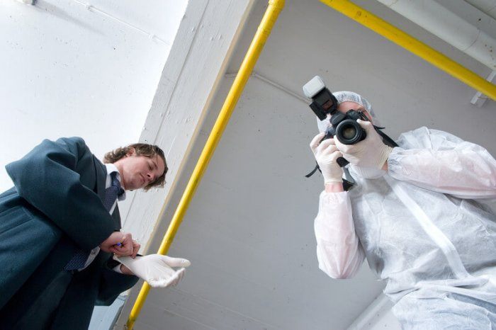 Detective standing over a body with a crime scene photographer standing next to him