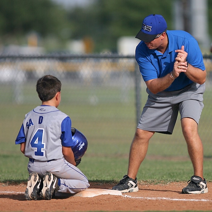 middle aged coach teaching a young boy to swing a bat in little league