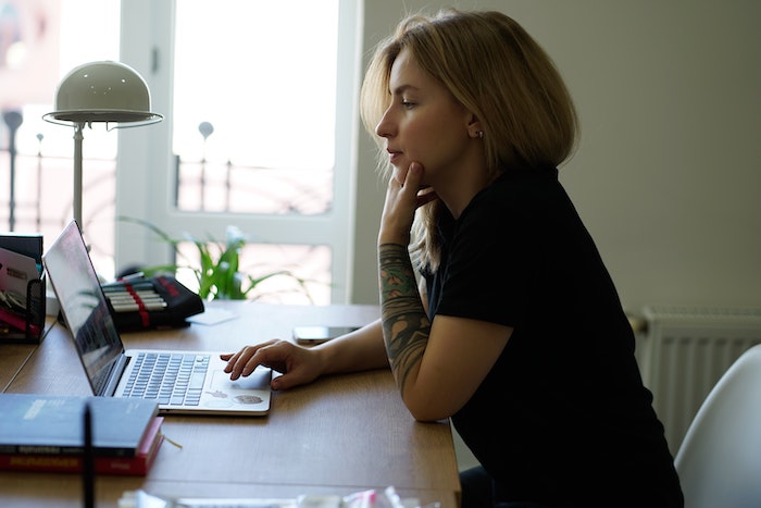 young woman with tattoos and bobbed colored hair looking at a computer thinking about what to write