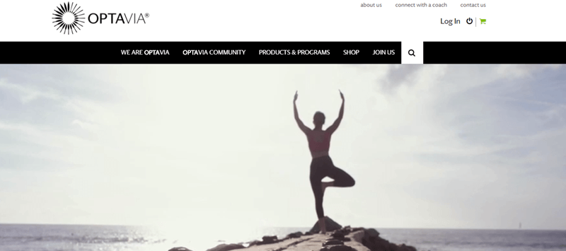 Optavia website screenshot showing an image of a young woman outside in front of the sea doing a yoga tree pose. 