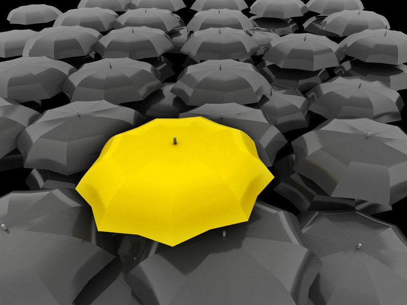 Stylized image of a collection of black umbrellas with one bright yellow one that is slightly higher