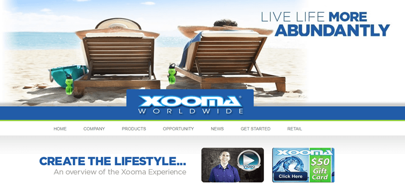 Xooma Worldwide website screenshot showing a slightly distorted image of a couple in reclining deck chairs on the beach, facing the water. 