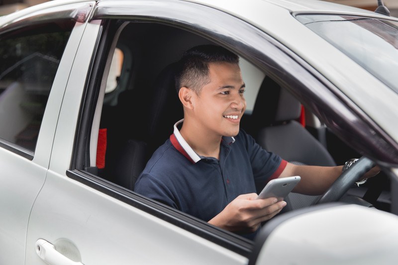 Image of a young man in a silver car using his phone making money doing rideshare