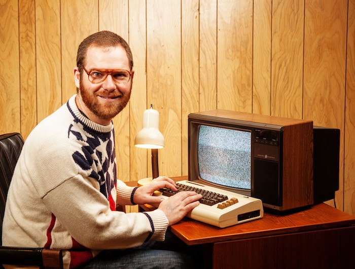 classic nerd trope photo of red hairded man with large glasses sitting at a 70's style computer with wood paneling in the background showing best nerd affiliate programs