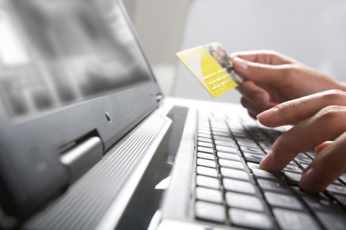 Hands on a keyboard with one holding a credit card