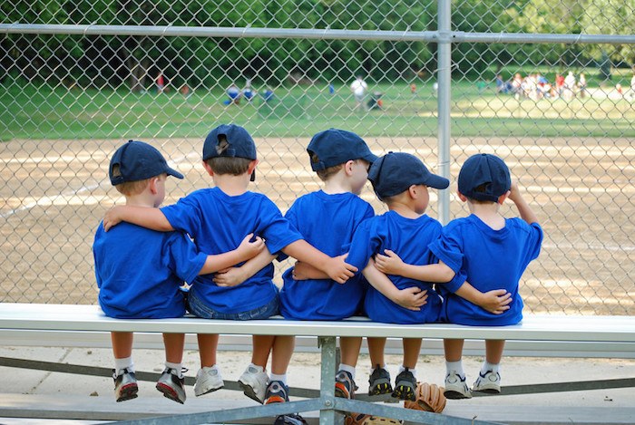 5 small boys sitting on a bench with baseball gear on representing the best baseball affiliate programs