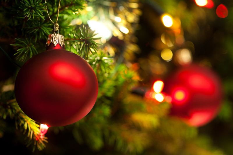 red glass christmas ball ornament closeup with christmas tree and lights in the background