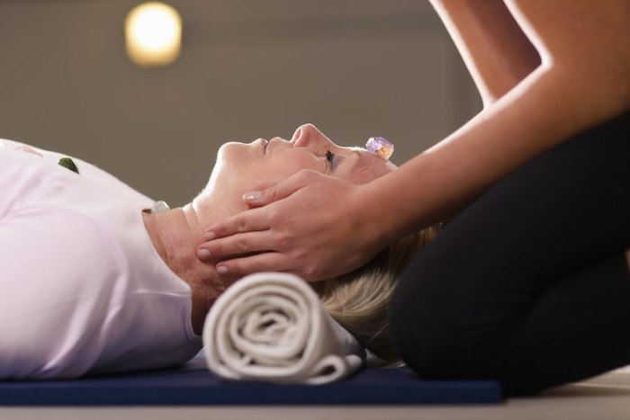 older woman receiving reiki treatment with hands being placed on her head