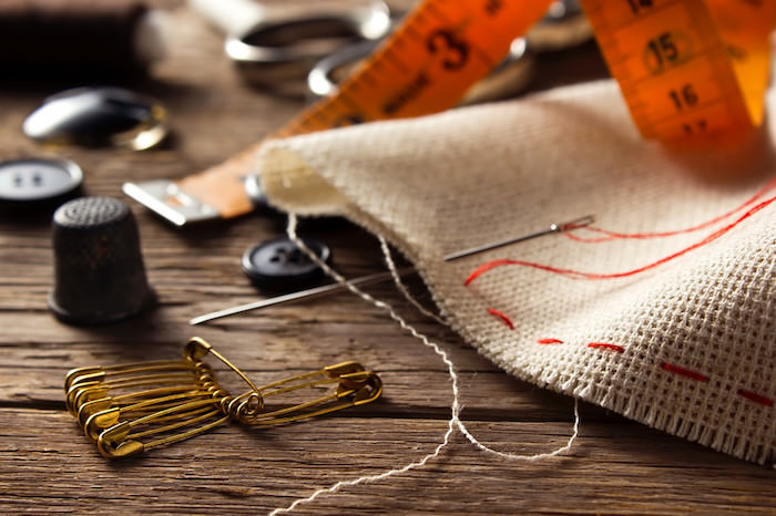 various sewing items including cloth, spool, needle, and thread on a wood table representing sewing affiliate programs