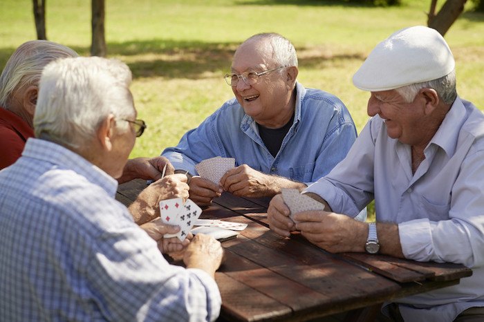 three old men and one old woman sitting at a table in the park playing cards to represent the best senior affiliate programs