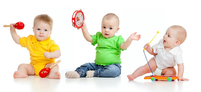 In this photo, three babies in bright colored clothing are playing with toys in front of a white background, representing the best baby clothes affiliate programs.