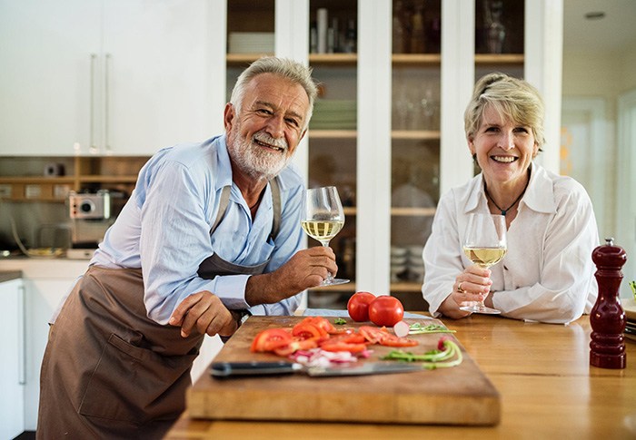 Older couple enjoying wine together in kitchen representing retired people who aren't ready to stop working