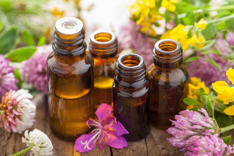 This photo shows an assortment of flowers and glass bottles on a wooden table.