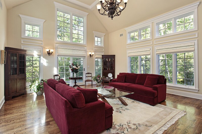 This photo shows two maroon-colored sofas with a light-colored rug in a room with high windows, representing the best affiliate furniture programs.