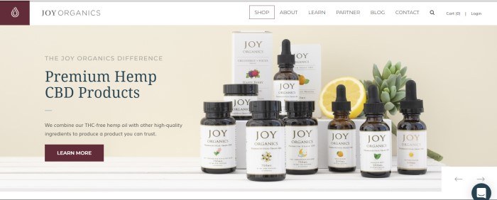 This screenshot of the home page for Joy Organics shows several bottles of CBD products, along with half a lemon and a succulent plant, in front of a beige background. 