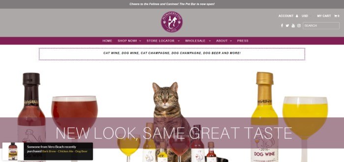 This screenshot shows a cat with several bottles and glasses of pet wine against a white background.