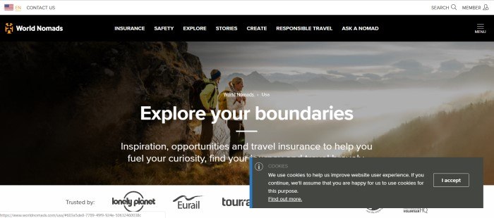 This screenshot of the home page for World Nomads shows a man and a woman on a trail overlooking a misty valley below them, with the words "Explore your Boundaries" in white lettering across it.