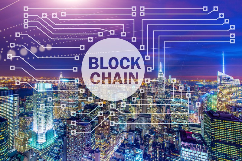 This picture shows a cityscape beneath a purple and blue sky with a 'blockchain' label and several lines linking different places on the picture, which suggests crypto-currency trading and represents the best blockchain affiliate programs. 