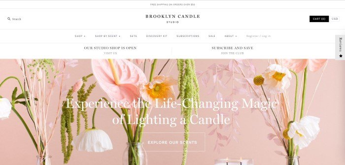 This screenshot of the home page for Brooklyn Candle Studio shows a pink background with pink and white flowers behind white lettering that reads "Experience the life-changing magic of lighting a candle."