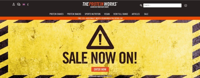  This screenshot of the home page for The Protein Works shows an image of what looks like a black and yellow hazard sign, with text in black lettering that reads 'Sale Now On!'