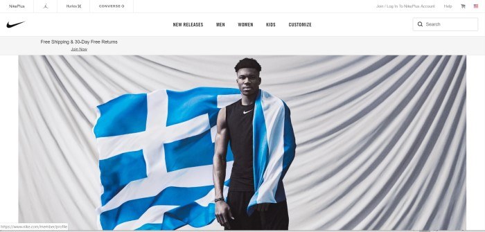 This screenshot of the homepage for Nike shows a young man wearing black Nike clothing with a blue and white flag draped around one shoulder and stretched behind him, standing in front of a large white cloth that's draped so the folds fall in a large u-shaped curve.