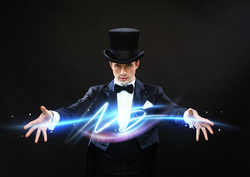 This photo shows a magician in a black suit, white shirt, black bow tie and black top hat, stretching out his arms while blue and purple lights extend from one hand to the other, representing the best magic affiliate programs.