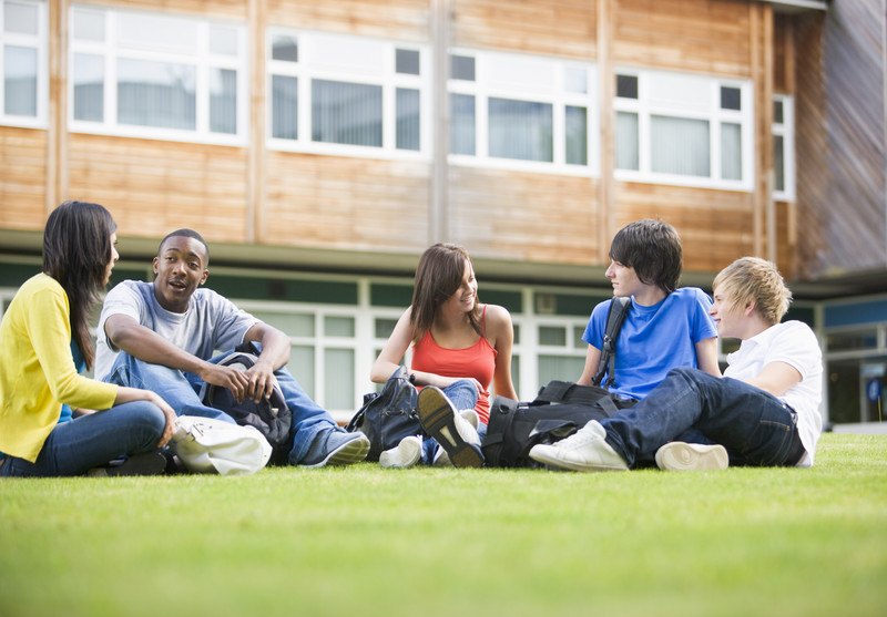 This photo shows a group of college students sitting and talking on a lawn outside what appears to be a university building, representing the best university affiliate programs.