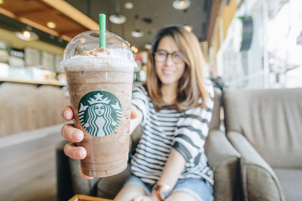 Happy young woman holding a cold Starbucks drink. You can join Wealthy Affiliate for less than a daily cup of Starbucks coffee. That's cheap!