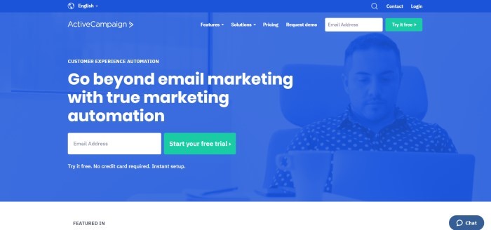 This screenshot of the home page for Active Campaign shows a dark filtered photo in royal blue of a man working at a laptop near a coffee mug, and white text that reads 'Go beyond email marketing with true marketing automation.'