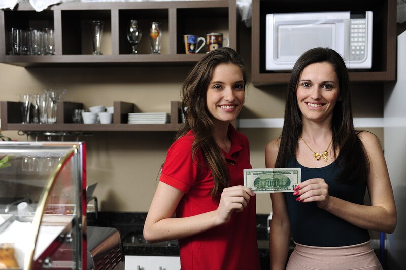 This photo shows two women business owners of a café holding cash and smiling near one of their pastry cases, representing the best business loan affiliate programs.