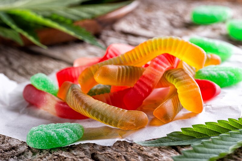 A pile of of marijuana gummy edibles sits on a rustic table near marijuana leaves, representing the best marijuana edibles affiliate programs.