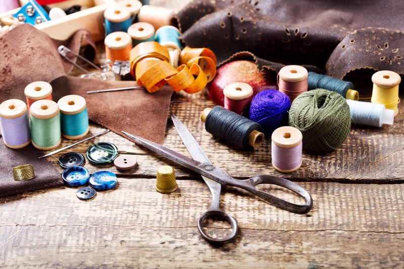 spools of yarn in multiple colors with a par of old scissors and buttons and needles