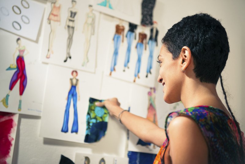 woman looking at fashion drawings on a wall comparing material with a potential sketch to use