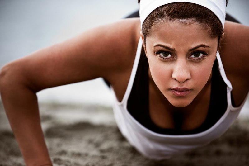 young woman staring intently at the camera doing a push up on the beach