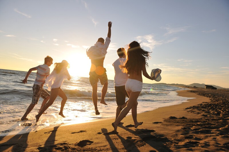 group of five people running on beach with light clothing and cheering