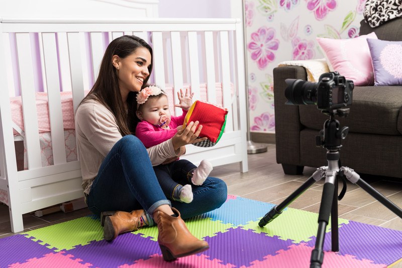 young woman with baby sitting in front of camera with plush toy