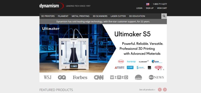 This screenshot of the home page for Dynamism has a gray background with a photo of a large 3D printer next to text in black lettering and several icons for companies that have used the printer or featured the printer in media.