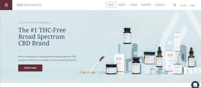 This screenshot of the home page for Joy Organics has a pale blue background with several Joy Organics products lined up near text in black lettering explaining more about the company and a brown call-to-action button for shopping.