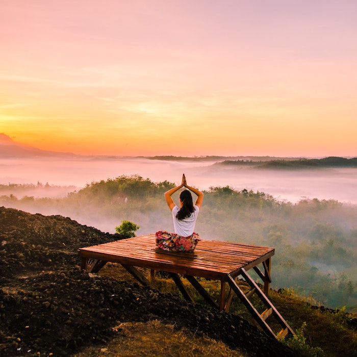 woman doing yoga on mountain deck with sunset in the background