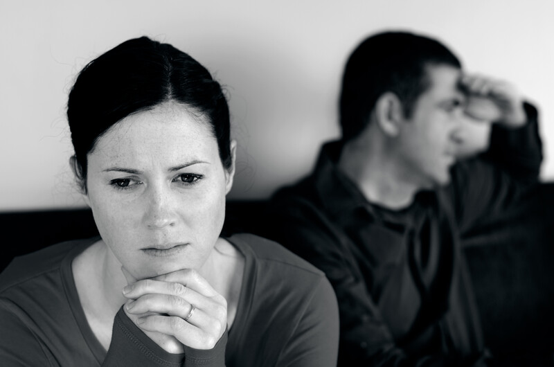 This black and white photo shows a sad or angry man and woman sitting beside each other on a couch, but not looking at each other, representing the best divorce affiliate programs.